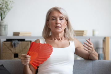 Tired mature woman suffering from heat at home, waving fan - obrazy, fototapety, plakaty