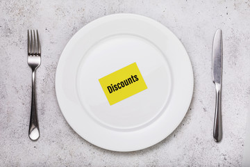 Tag with the inscription discounts in a white plate on the table, top view