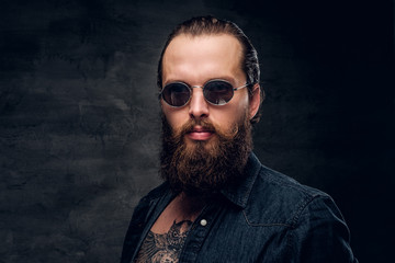 Portrait of brutal bearded man in sunglasses at dark photo studio.