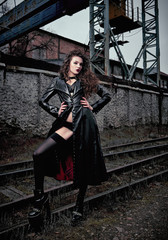 Fashion shot: portrait of sexy cute goth girl (informal model) in leather coat, stockings and lingerie standing at railroad (industrial area)