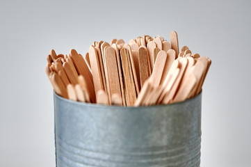Close up of wooden stirrers in a tin cup on white background