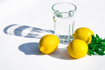 Lemons, fresh green mint and a glass glass with water on a white background. Shadows on a white background