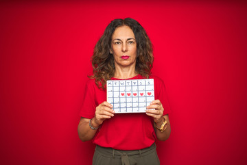 Middle age senior woman holding menstruation calendar over red isolated background with a confident expression on smart face thinking serious