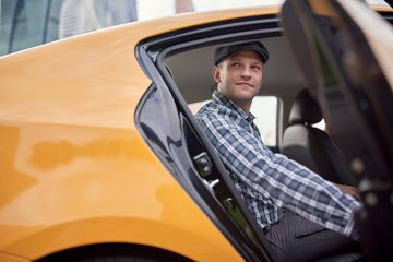 Picture of young man in cap and plaid shirt sitting in back seat in yellow taxi