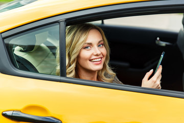 Photo of young blonde with phone in her hand sitting in back seat of yellow taxi