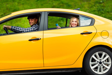 Photo of young woman with phone in her hands sitting in back seat of yellow taxi with driver.