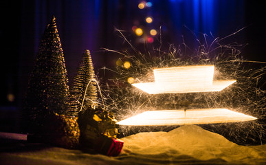 Glittering burning sparkler on snow with blurred Christmas tree on dark background. New Year Holiday concept with empty space for your text