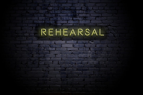 Highlighted brick wall with neon inscription rehearsal