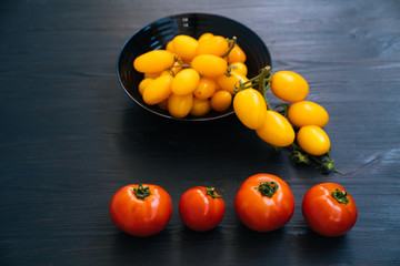 Top view of yellow and red cherry tomatoes in bowl on black wooden background