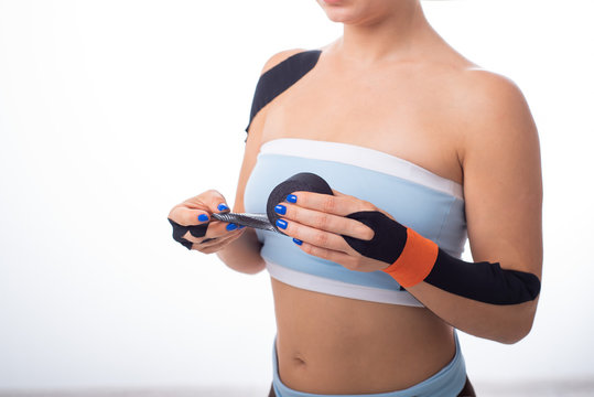 Female athlete puts a teip on her wrist. Kineziology, alternative treatment for injuries of joints and tendons. A woman is holding a roll of kineziotape. Lymphatic drainage. Close up.