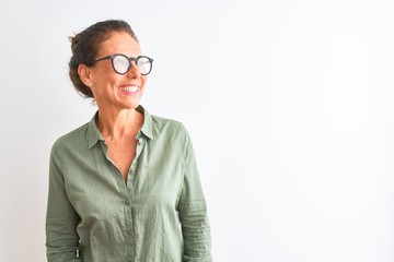 Middle age woman wearing green shirt and glasses standing over isolated white background looking away to side with smile on face, natural expression. Laughing confident.