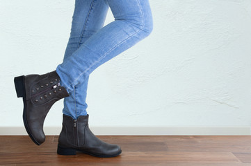 Legs of a girl in blue jeans and brown boots close-up. Against the background of a white wall.