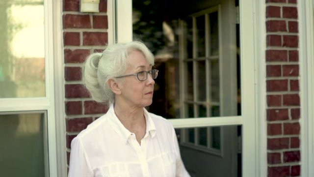 A mature woman walks quickly out of the backdoor of her home as if looking for something or someone.