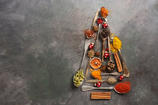 Various spices in spoons in the shape of a Christmas tree on a dark rustic background. Top view, flat lay, copy space.