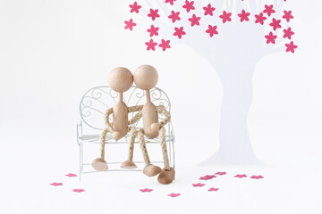Two figurines sitting on a bench under a paper cherry tree and hug each other landscape format