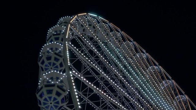 Night view of the ferris wheel. Bright multi-colored lights. Amusement park.