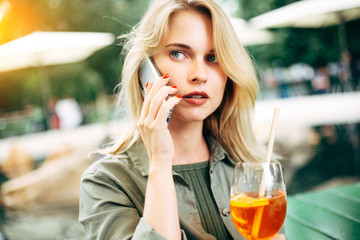 Photo of blonde with cocktail in her hands talking on phone on street.