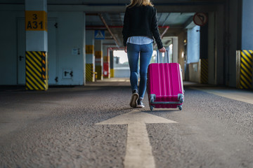 Photo from back of blonde with pink luggage walking along passage at airport.