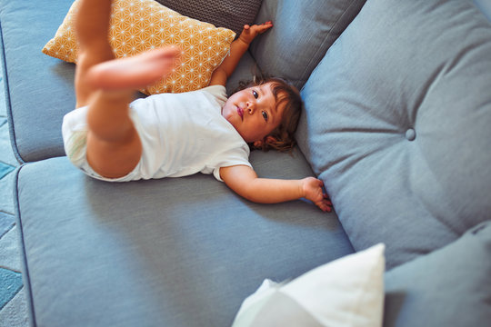 Beautiful toddler child girl wearing white bodysuit lying down on the sofa