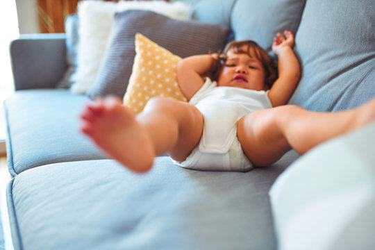 Beautiful toddler child girl wearing white bodysuit lying down on the sofa