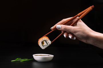 Hand holds sushi over bowl with soy sauce