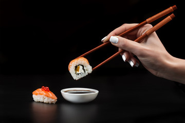 Hand holds sushi over bowl with soy sauce
