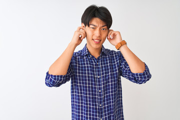 Young chinese man wearing casual blue shirt standing over isolated white background covering ears with fingers with annoyed expression for the noise of loud music. Deaf concept.