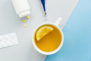 Fototapeta na wymiar Cold and flu season. Cup with hot tea and lemon, thermometer, pills on a light background. Treatment and prevention of the virus. Copy space