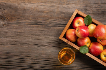 Ripe red apples in wooden box with glass of fresh juice on a wooden table