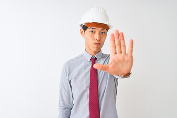 Chinese architect man wearing tie and helmet standing over isolated white background doing stop sing with palm of the hand. Warning expression with negative and serious gesture on the face.