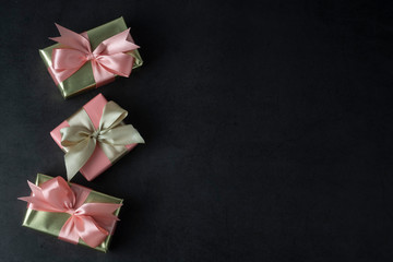 Party, birthday present in golden box with pink bow on black background. Top view or flat lay. Copy space.