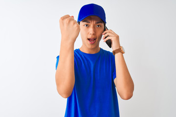 Chinese deliveryman wearing cap talking on the smartphone over isolated white background annoyed and frustrated shouting with anger, crazy and yelling with raised hand, anger concept