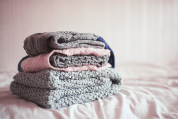 Stack of knitted clothes in bed close up. Winter season. Selective focus.