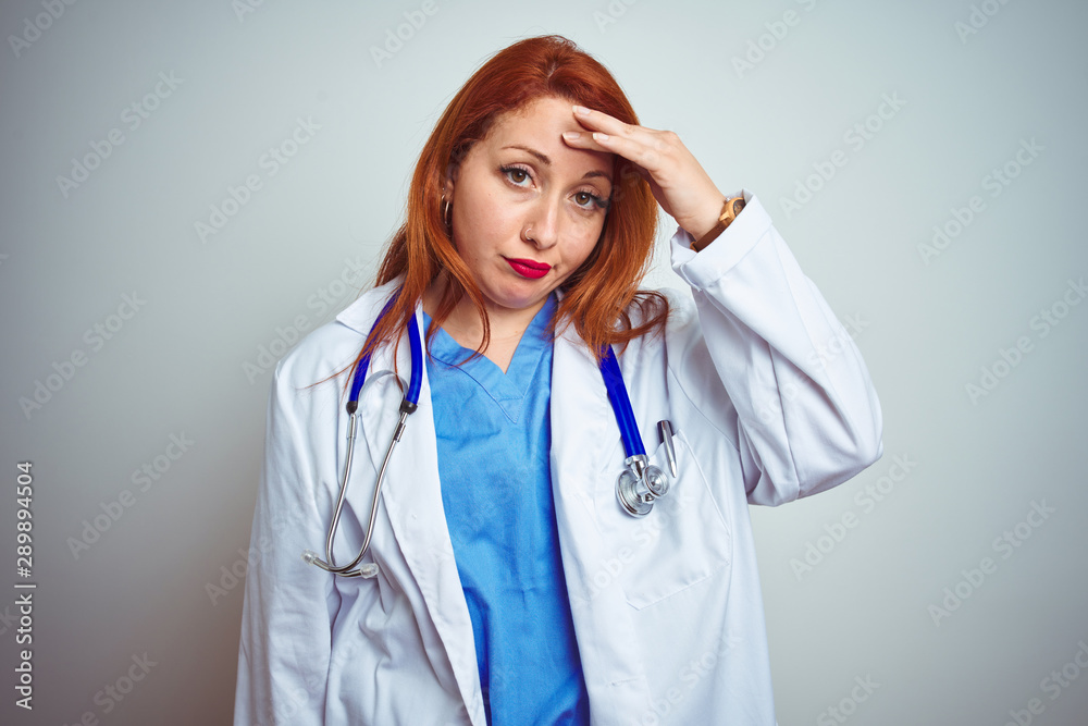 Sticker Young redhead doctor woman using stethoscope over white isolated background worried and stressed about a problem with hand on forehead, nervous and anxious for crisis