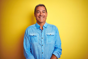 Handsome middle age man wearing denim shirt standing over isolated yellow background with a happy and cool smile on face. Lucky person.