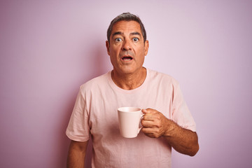 Handsome middle age man holding cup of coffee standing over isolated pink background scared in shock with a surprise face, afraid and excited with fear expression