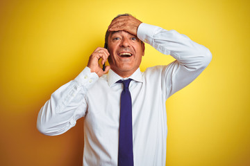 Middle age businessman talking on the smartphone over isolated yellow background stressed with hand on head, shocked with shame and surprise face, angry and frustrated. Fear and upset for mistake.