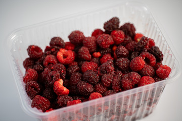 A lot of fresh raspberries in plastic packaging on a white background