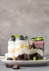 Three layered desserts with vanilla and chocolate cake, whipped cream and blackberries in mason jars.