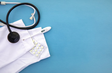 a stethoscope next to a medical gown lie on a blue background next to a thermometer