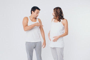 Fototapeta premium pregnant woman and man in sportswear on white background. The girl holds her stomach with her mouth wide open and a surprised on her face