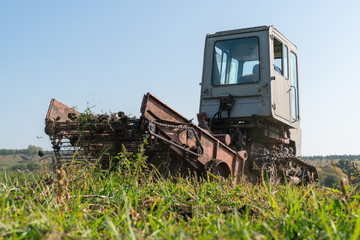Fototapeta premium An old tractor rides across a field and harvests potatoes