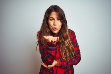 Young beautiful woman wearing red t-shirt and jacket standing over white isolated background looking at the camera blowing a kiss with hand on air being lovely and sexy. Love expression.