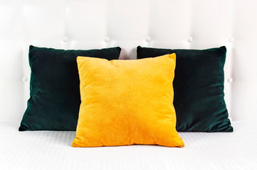 Bright decorative soft pillows in bed on the background of leather quilted headboard. Emerald and orange pillow, part of bed close-up, comfort. Quilted headboard background, interior