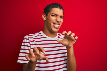 Young handsome arab man wearing striped t-shirt over isolated red background smiling funny doing...