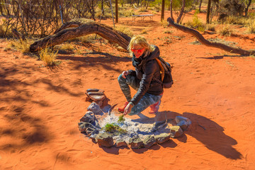 Tourist woman burns of bush plants on a fire surrounded by traditional stone. Plants have special properties and during the smoking ceremony of the Indigenous Australians are burned to purify.