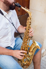 Naklejka premium Close up of a man sitting at the door of a building on the street holding his saxophone