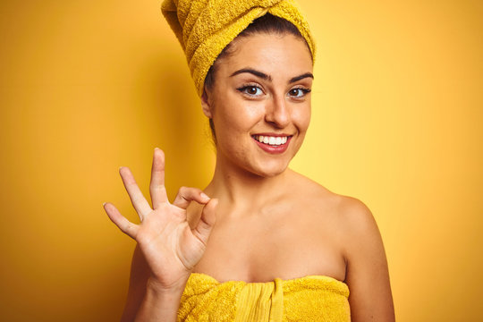 Young beautiful woman wearing towel after shower over isolated yellow background doing ok sign with fingers, excellent symbol