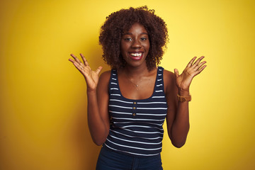 Young african afro woman wearing striped t-shirt over isolated yellow background celebrating crazy and amazed for success with arms raised and open eyes screaming excited. Winner concept