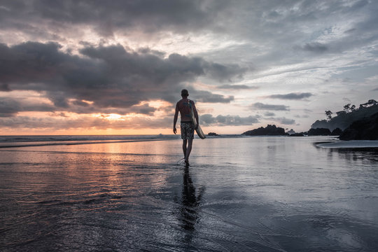 Hombre camina por la playa de colombia hacia el oc&eacute;ano pac&iacute;fico para surfear al atardecer. 